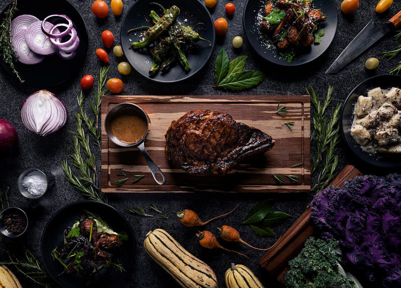 A moody overhead shot of a steak surrounded by sides and ingredients