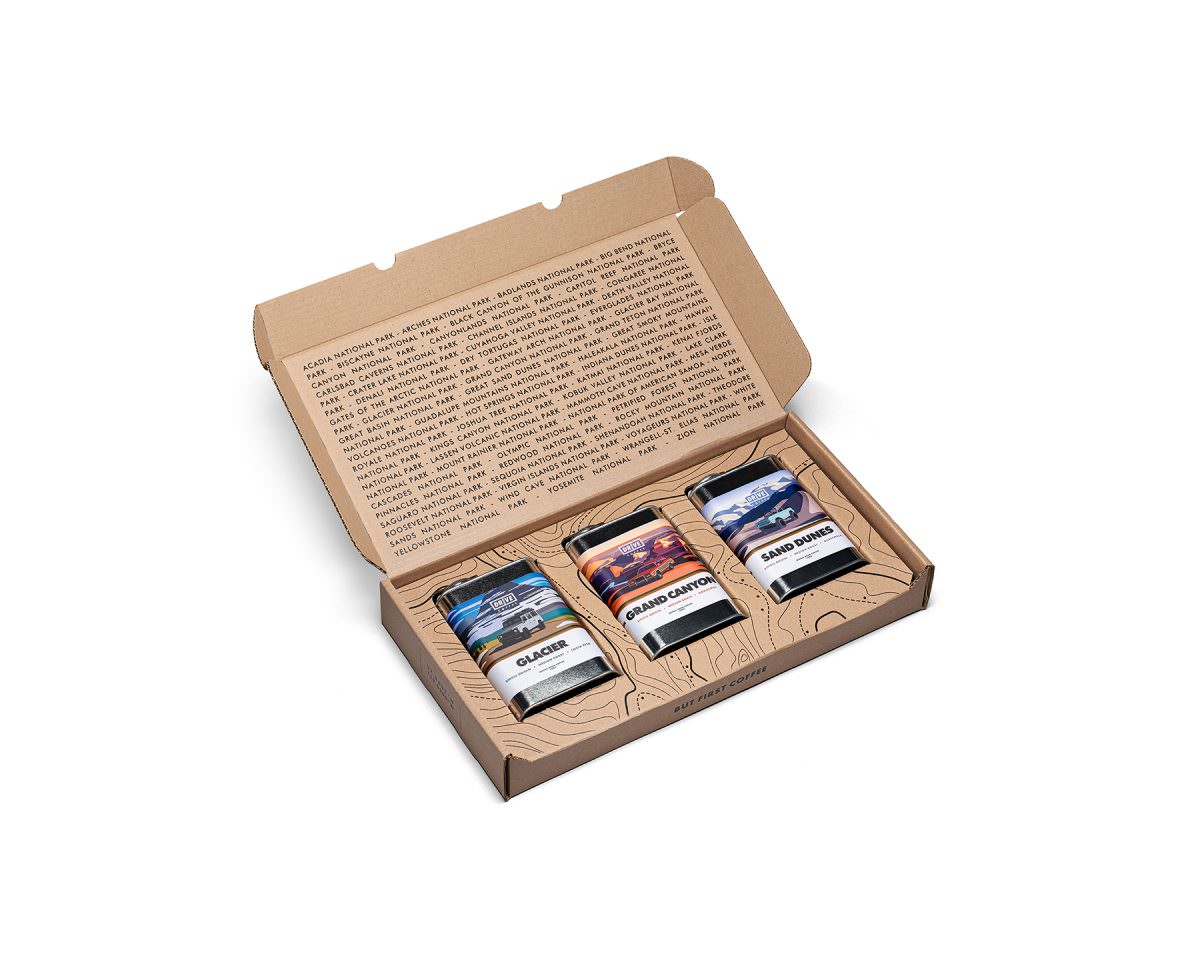 An opened box view of the Drive Coffee National Parks box set revealing 3 coffee tins — Glacier, Grand Canyon, and Sand Dunes