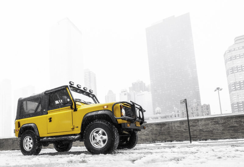 An alternate view of the Land Rover Defender with a snowy backdrop of tall buildings