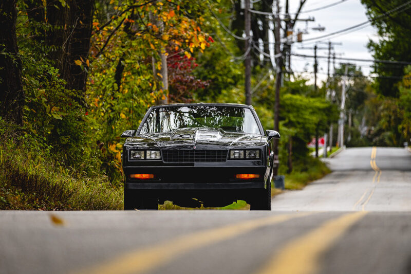 A picture of a Monte Carlo SS from the front pulled over to the side of a mildly winding road with fall foliage