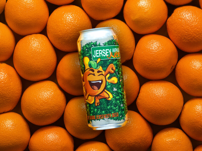 1 can of Jersey Ave Juice IPA Beer resting on a floor of oranges, showcasing the label design