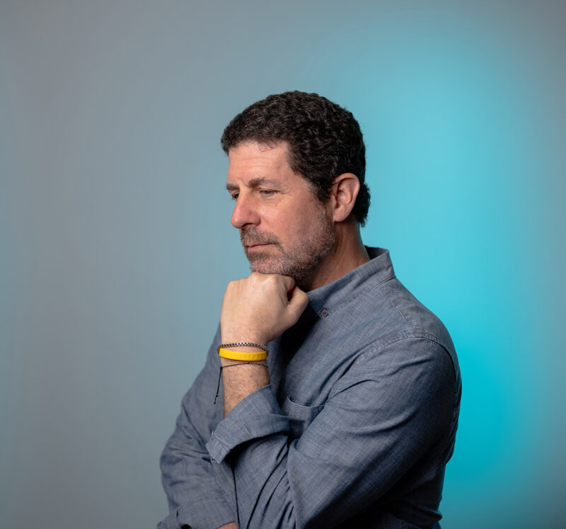 A portrait of a man in the thinker pose featuring a blue LED light filling in the right side of the grey background