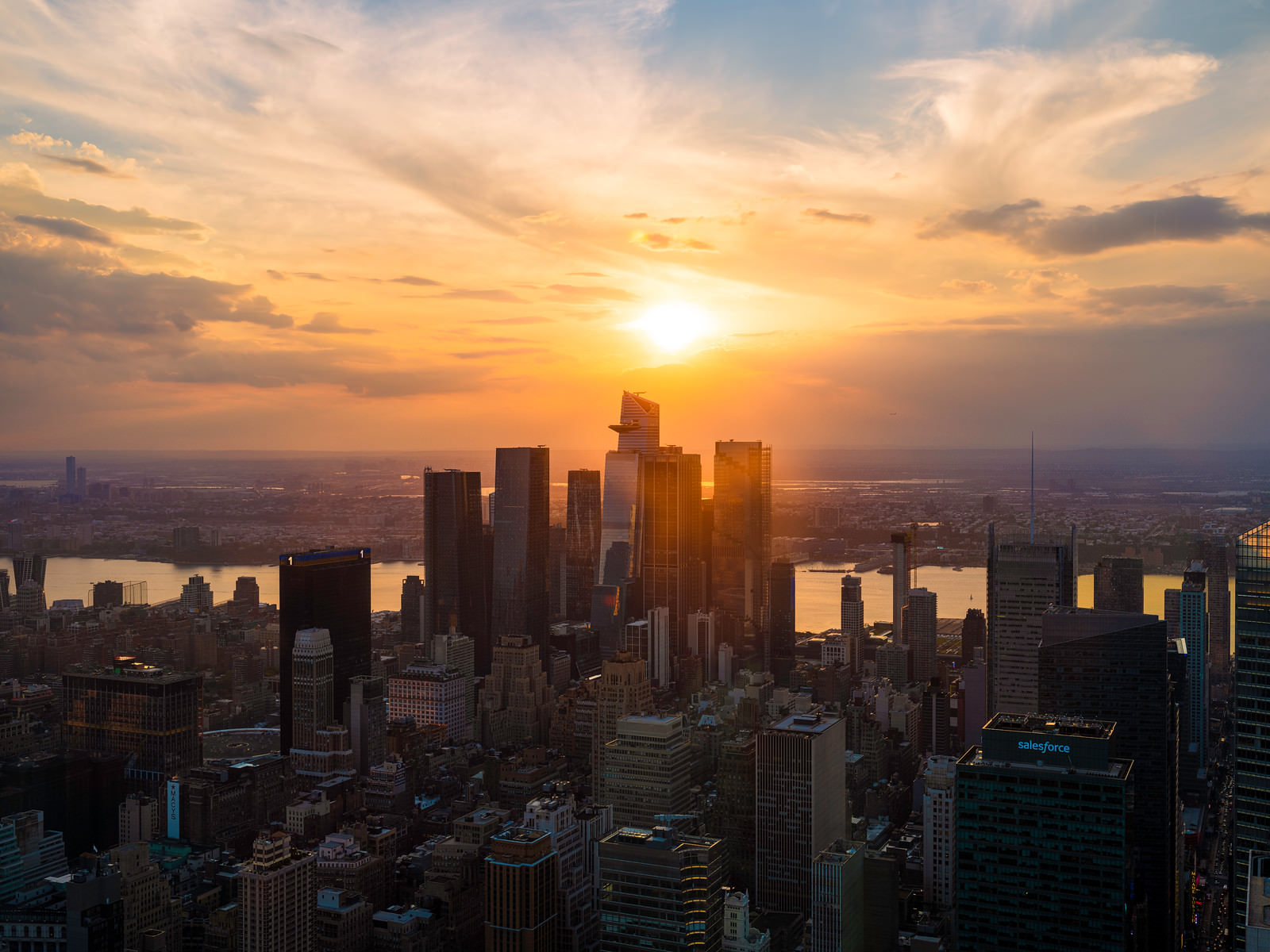 the Hudson yards skyline at sunset. The sun is setting JUST above the buildings and is very bright and colorful.