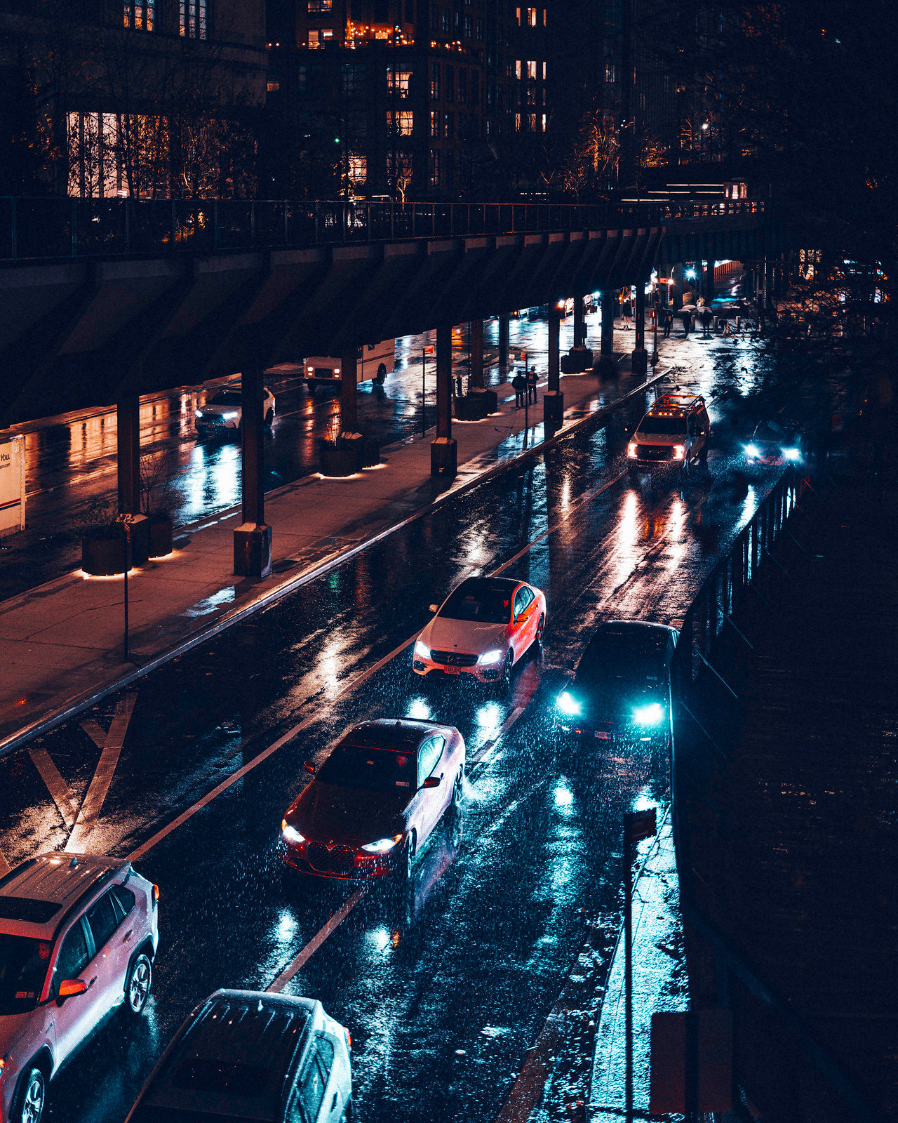 A rainy new york scene showing cars driving down a highway, captured from a bridge above. It features a dark and moody color grade.