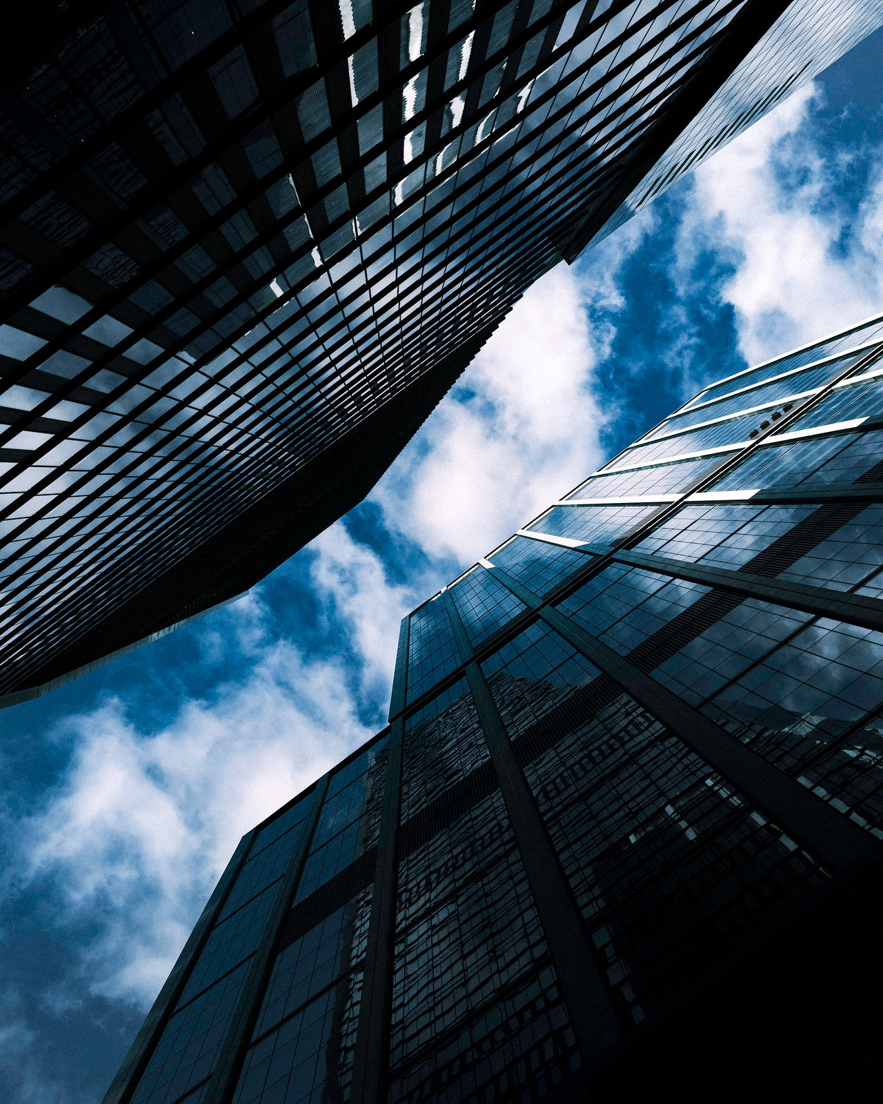 A looking up photo of two buildings in nyc - the sky is very blue and the buildings are largely made of glass.