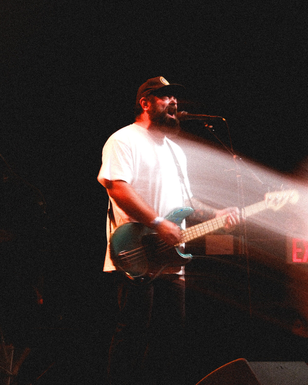 Guitarist in a white shirt singing into a microphone with bright light beams.