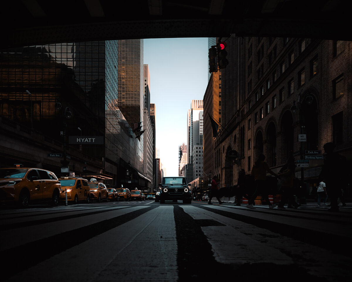 Street-level view of 42nd Street in Manhattan, with yellow cabs and a Jeep crossing a wide striped intersection.