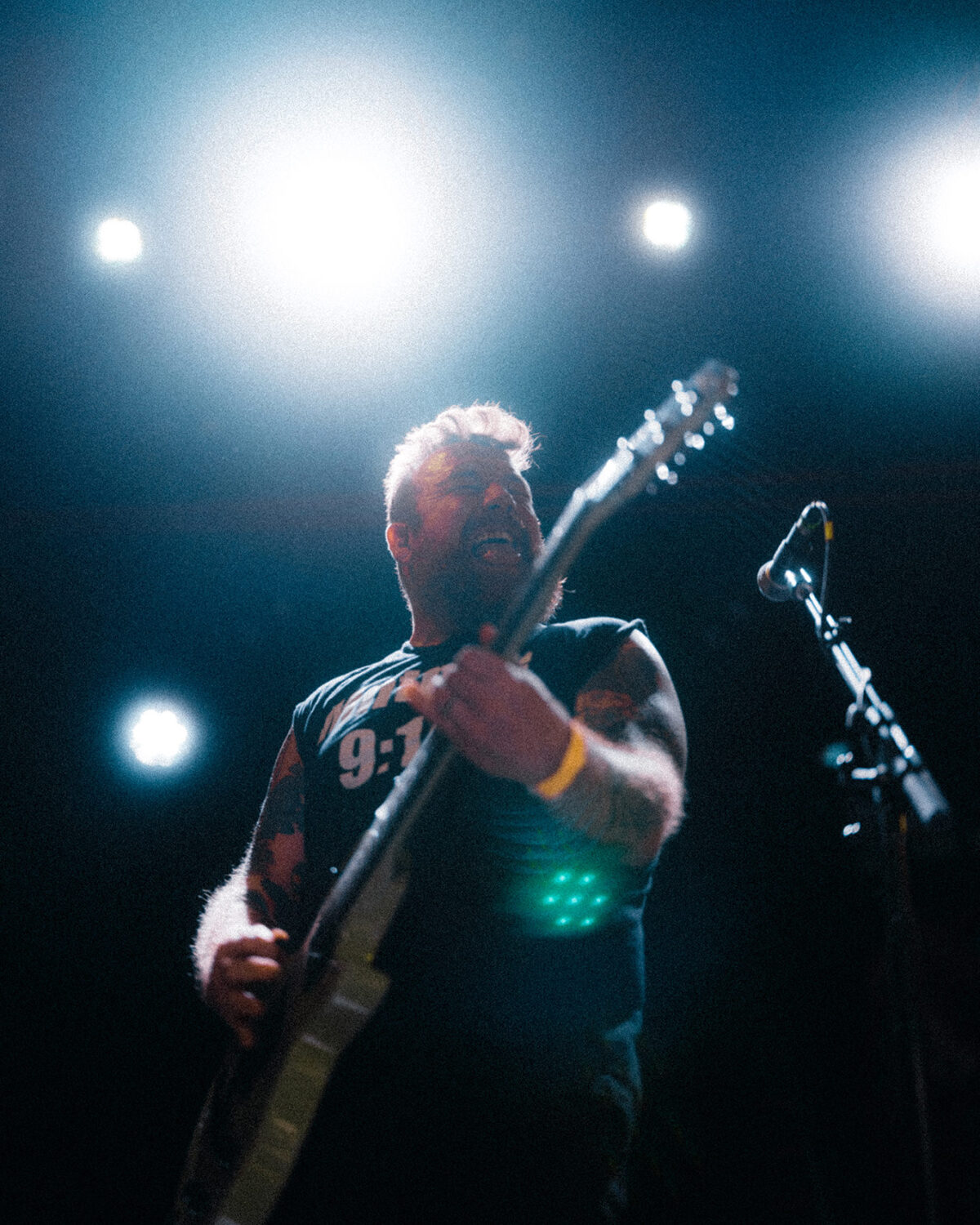Singer-guitarist playing with a wide grin under bright overhead lights.