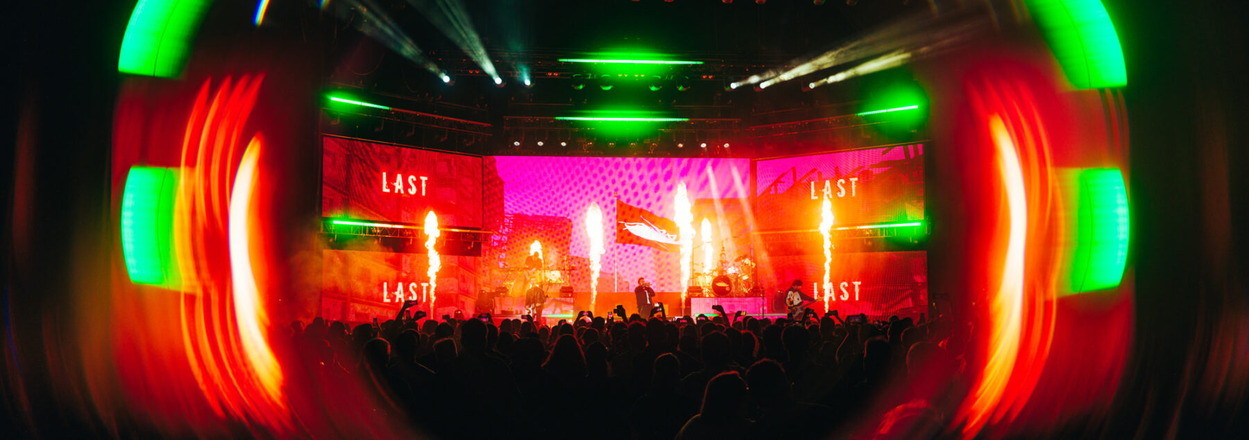 Wide fisheye view of stage with pyro and green/red lighting.