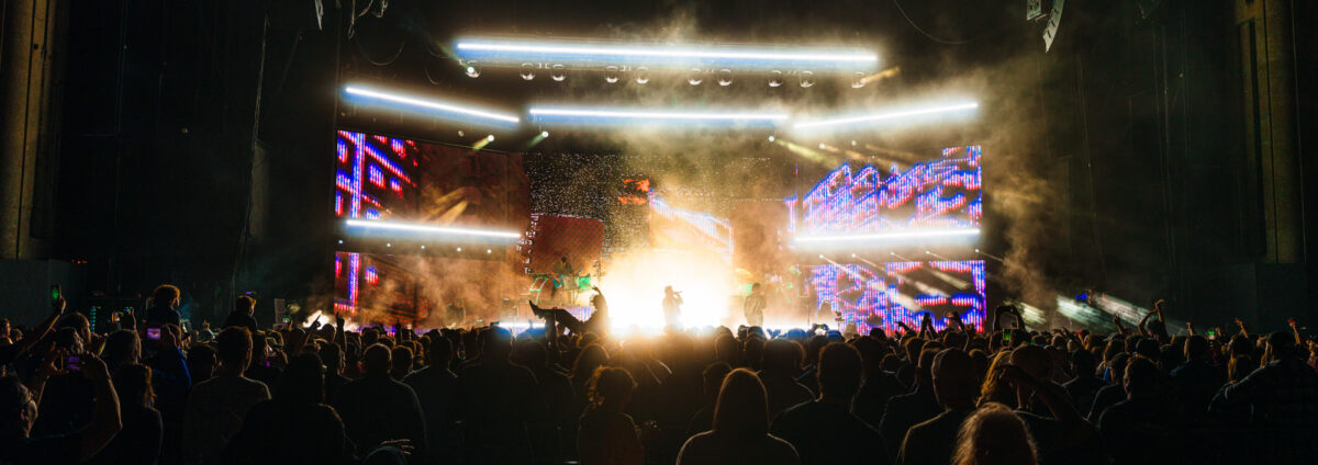 Wide crowd view of full stage with lights and pyro.