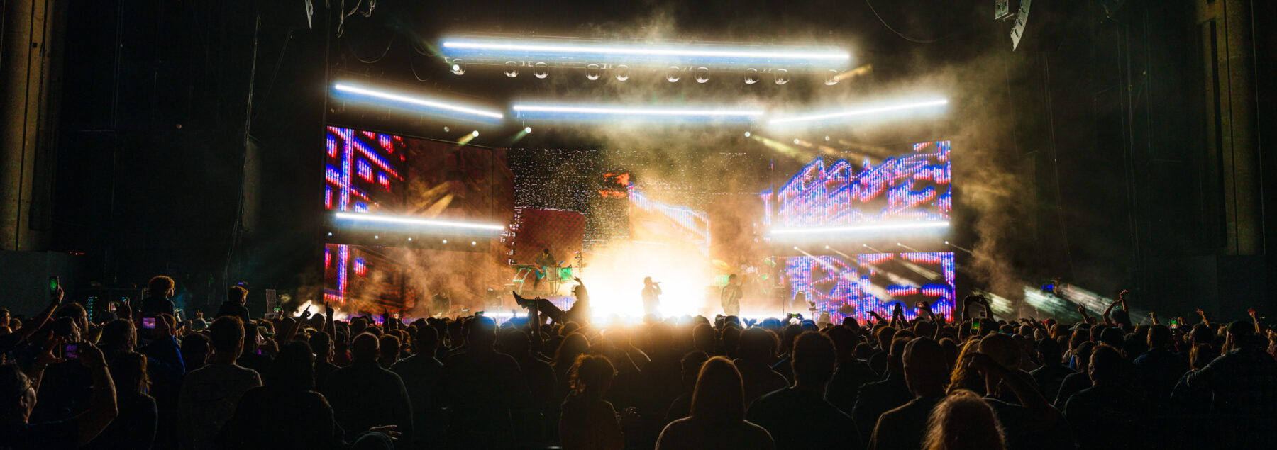 Wide crowd view of full stage with lights and pyro.