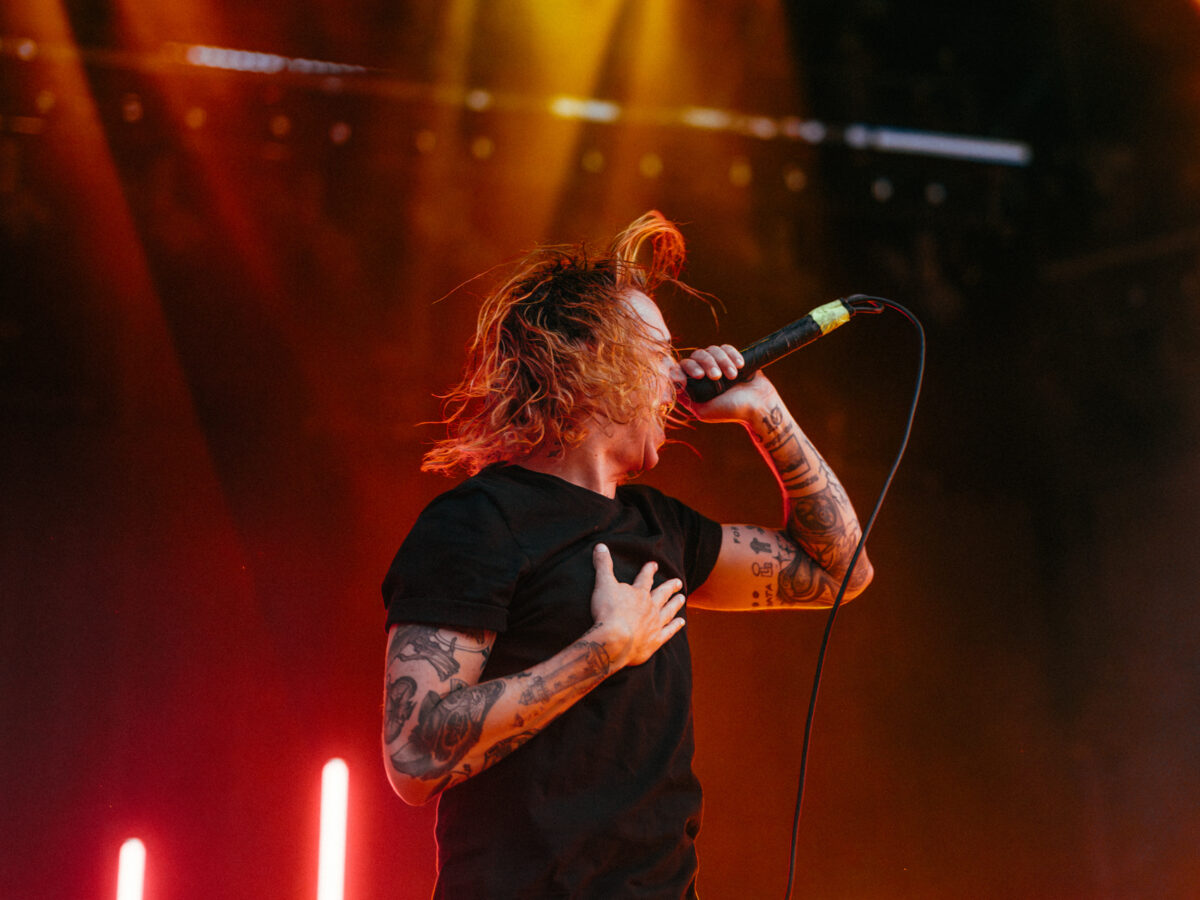 Vocalist screaming with hand on chest under red/yellow light.