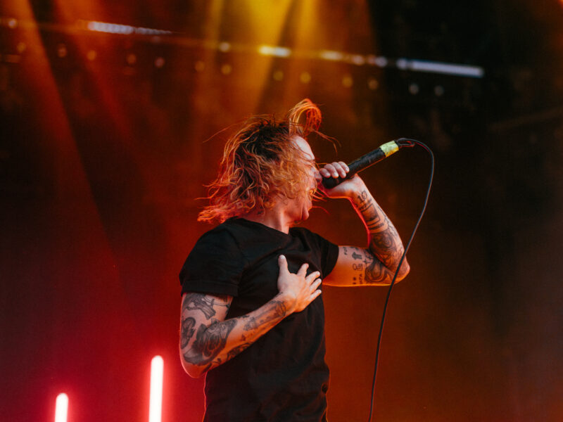 Vocalist screaming with hand on chest under red/yellow light.