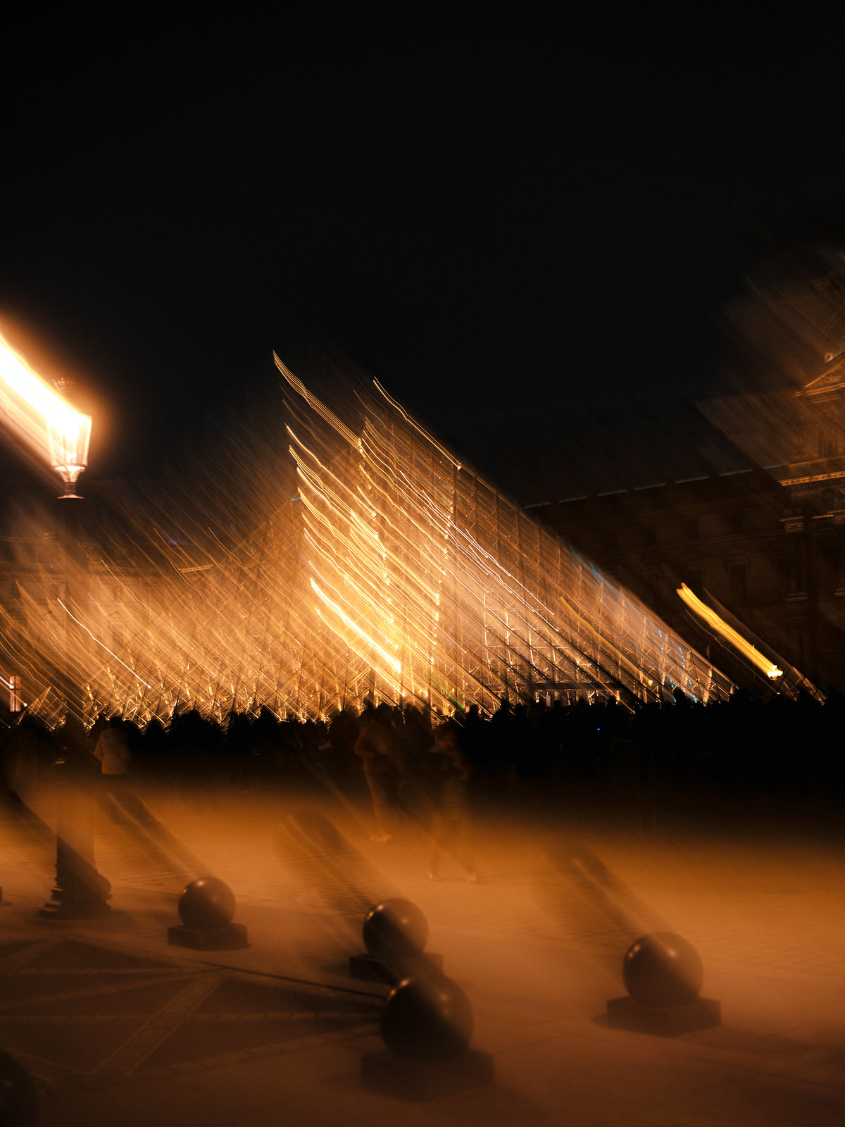 The lourve at night in a yellowly orange color with a shutter drag blurry effect