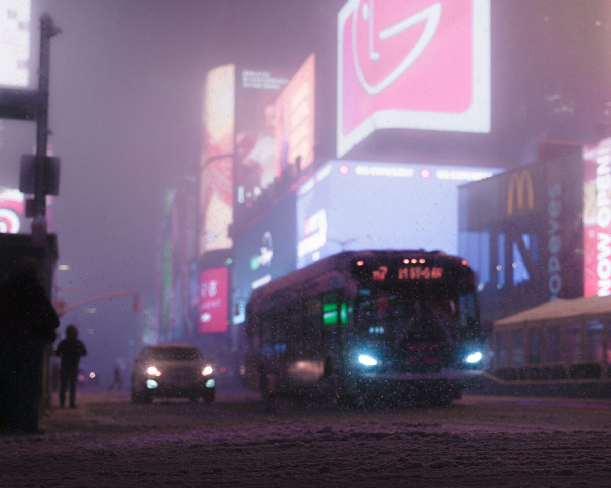 A snowy scene at night in time square with a bus and traffic driving down a street