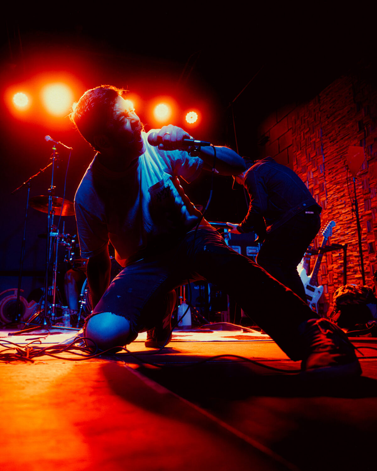 Sparks The Rescue singer kneeling on stage with microphone under glowing red lights at The Wood Shop in Brooklyn NYC