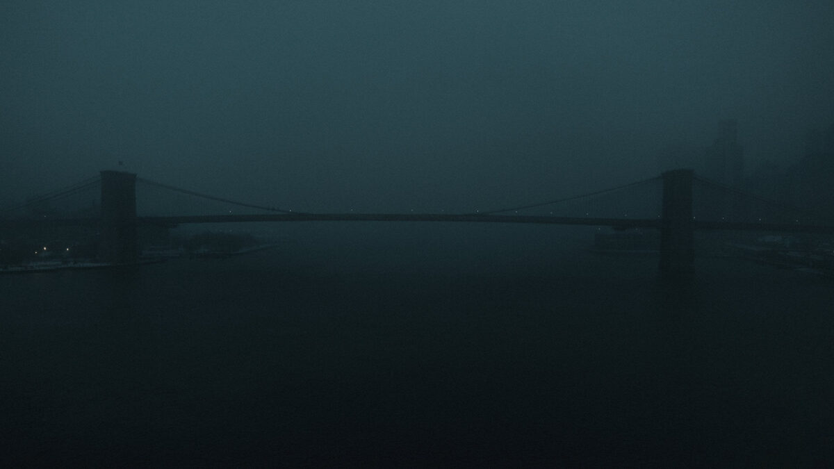 The Brooklyn Bridge fading into dense snowfall above the East River during a New York winter storm.