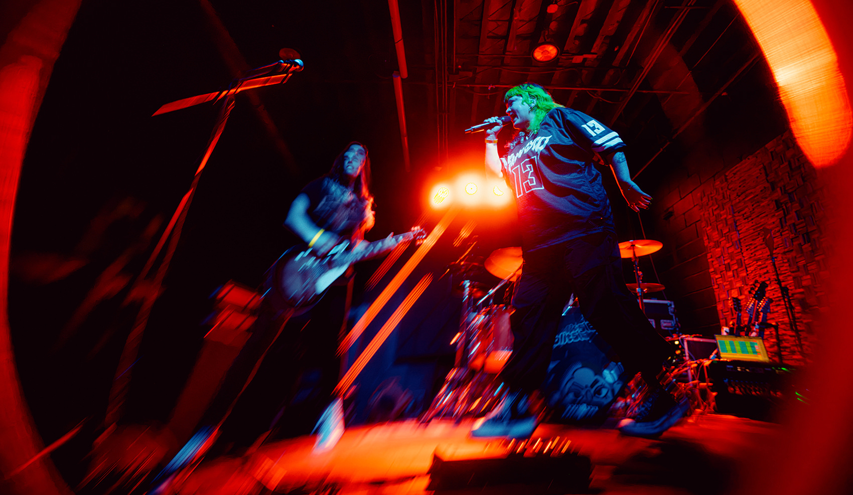 Fisheye view of Lolitslea performing at The Wood Shop in Brooklyn, vocalist and guitarist framed together under warm red stage lighting.